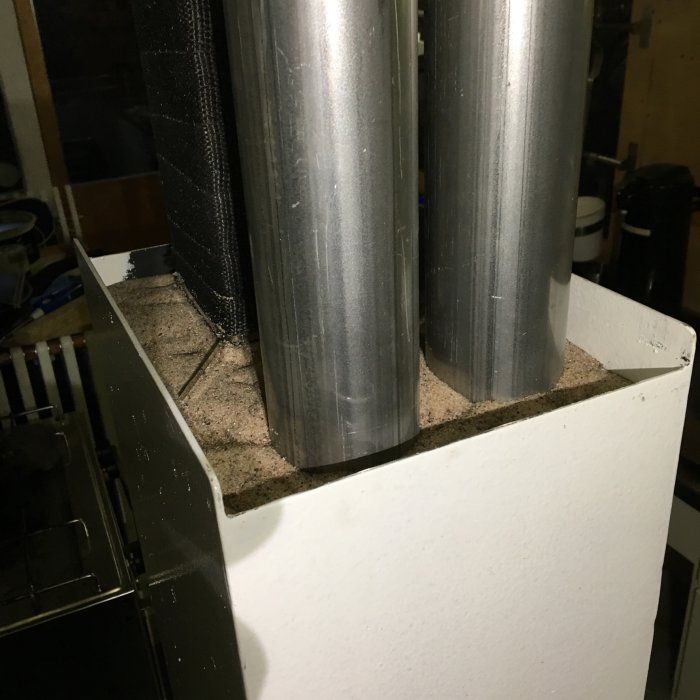 Bild på skorsten med meterrör monterade i kasse fylld med sand, omgiven av isolering.