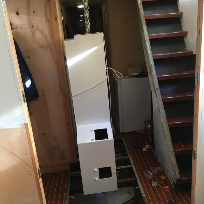 Stor vit metallkamin som hänger i kedja på ett byggprojekt nära en trappa och verktyg på golvet.