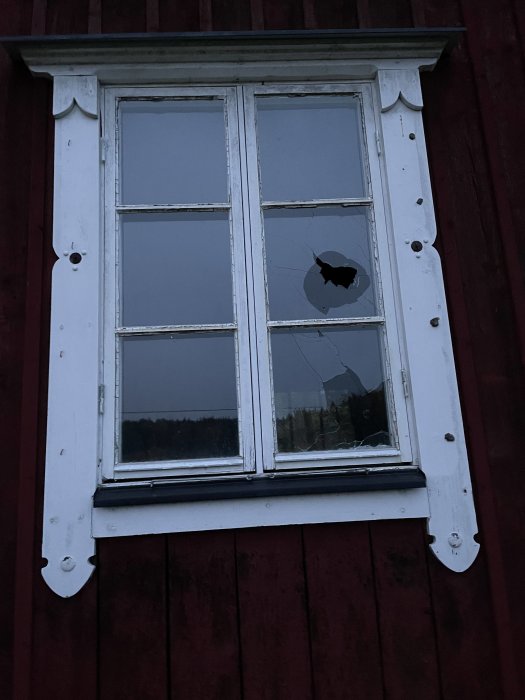 Gammalt 80-tals tvåglasfönster med en krossad ruta på en rödmålad trävägg.