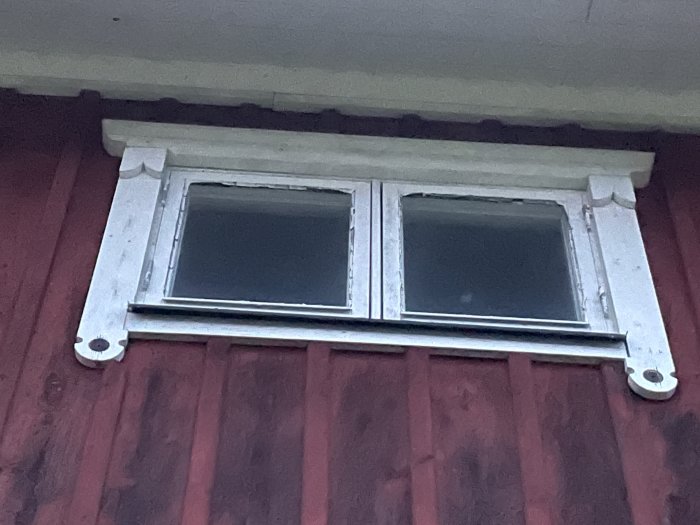 1980-tals tvåglasfönster på en röd vägg, behöver reparation men är i relativt gott skick.