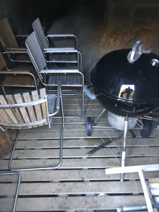 Krypgrund med trädeck och grill, stolar staplade, klippan i bakgrunden.