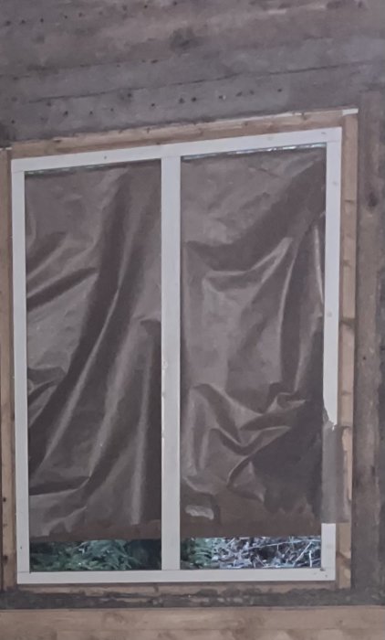 Fönster utan tätningslist, täckt direkt med presenning mot en karm i en oisolerad vägg.