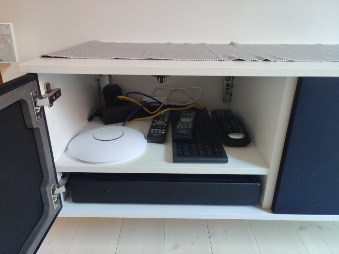 Router, server och annan nätverksutrustning samt fjärrkontroller på en hylla inomhus.