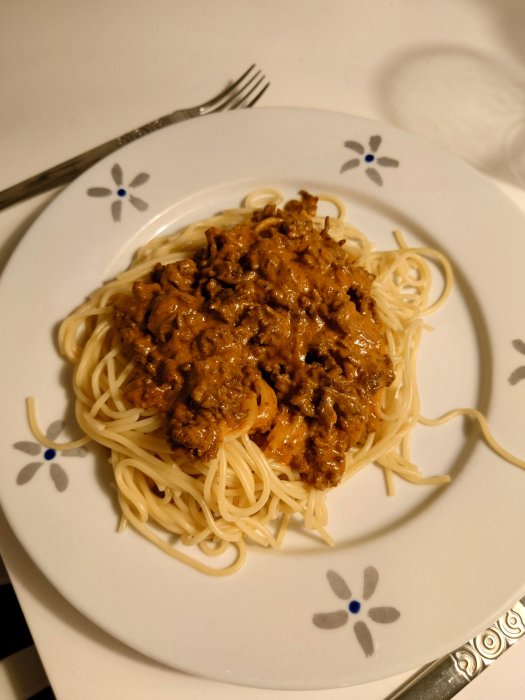 Hemlagad köttfärssås serverad på spaghetti på en vit blommönstrad tallrik med en gaffel.