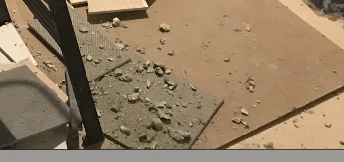 Golv under renovering med damm och spillt fixmedel på kakelplattor.