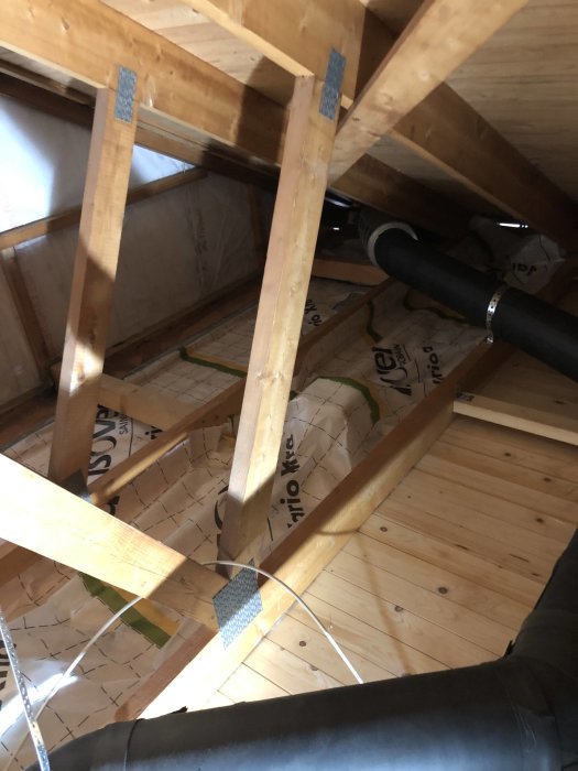 Installation av ny ångbroms mellan träbjälkar på en vind med synlig isolering och trägolv.