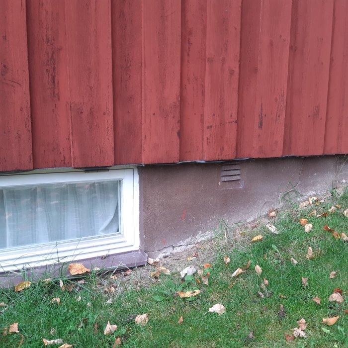 Husfasad där röd panel övergår i källarvägg med synlig isolering och ett ventilgaller.