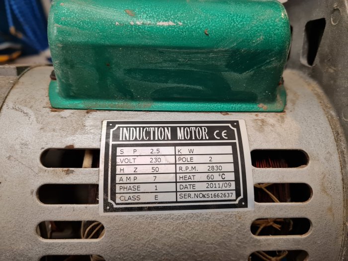 Kompressormotor med specifikationsetikett och tecken på skador på lindningarna.