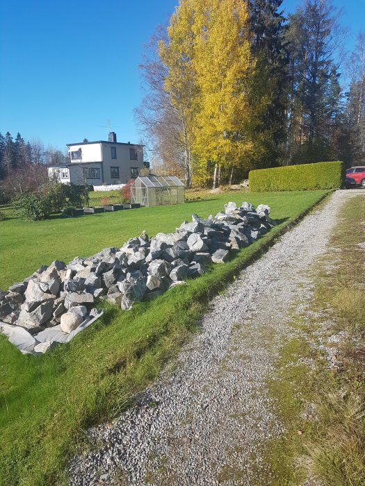 Stora stenblock spräckta i mindre bitar vid en grusgång med ett hus och trädgård i bakgrunden.