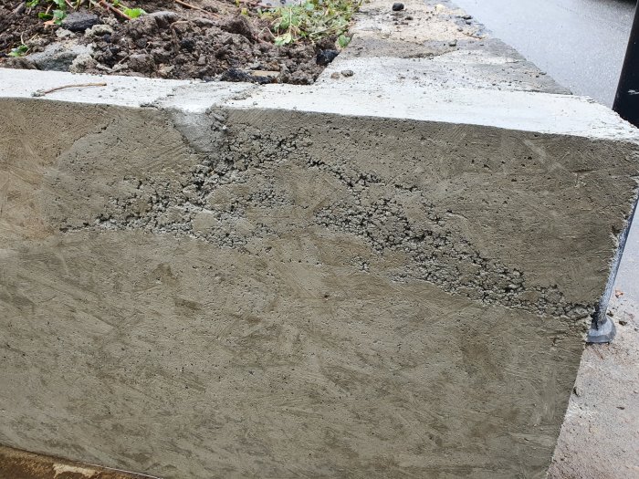 Närbild av en nyligen gjuten betongstödmur med synliga håligheter och ojämnheter.