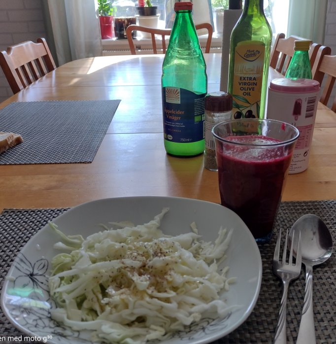 Frukostbord med tallrik vitkål och dressing, glas med morot- och rödbetsjuice, äppelcidervinäger och olivolja i bakgrunden.