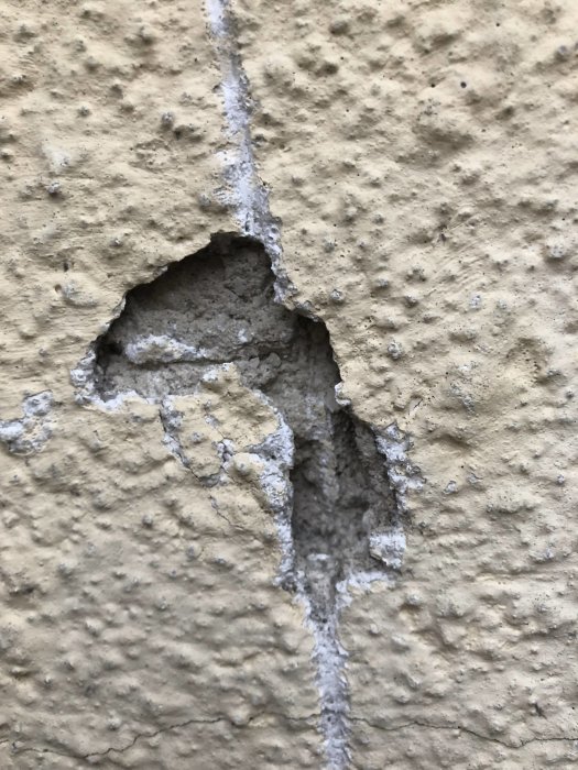 Skada på äldre kalkputsad fasad med sprickbildning och en större avslagen del.