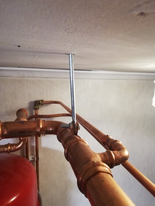 Kopparledningar med en lös rörklammer som inte är åtdragen mot taket i ett värmeinstallationssystem.