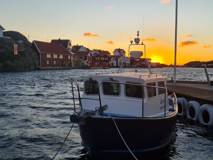 Solnedgång vid Klädesholmen med båt i förgrunden och traditionella röda hus i bakgrunden.