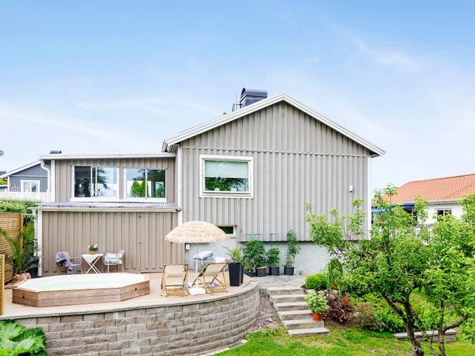 Ett modernt grått enplanshus med en träterrass och trädgård.