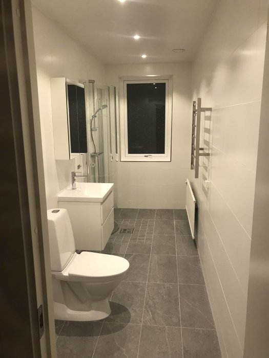 Renoverat badrum med toalett, handfat, dusch och handdukstork, i väntan på installation av maskiner.