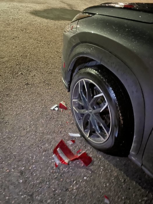 Bilparkering med krossat rött bakljus och skrapor på en bil i natten.
