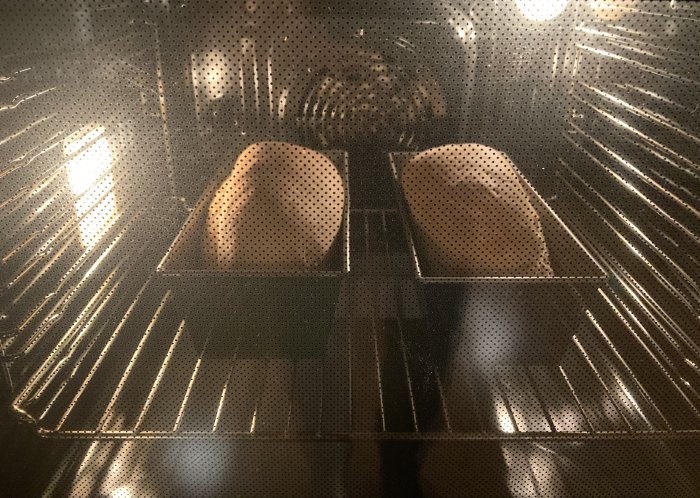 Två bröd bakas i ugn på metallgaller, sett genom ugnsglaset.