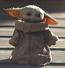 Förslag på alt-text: "Leksak av karaktären Baby Yoda som står på en träyta.