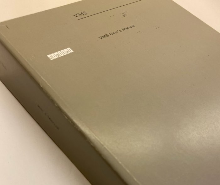 Grå bok med titeln "VMS User's Manual" på framsidan som ligger på ett vitt bord.
