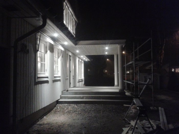 Trappsteg med betongentré upplysta av överliggande ljus, ställning till höger i bild.