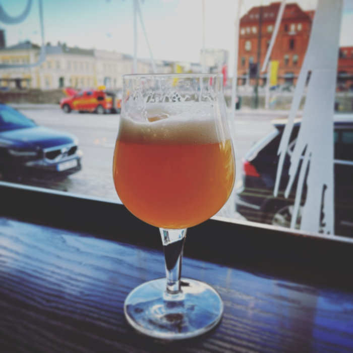 Ölglas med skummande dryck framför ett fönster med utsikt över gatan och bilar.