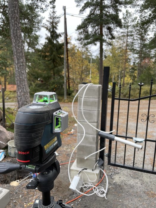 Nivelleringslaser framför ett staket med nyligen dragen elektrisk kabel i ett utomhusbyggprojekt.
