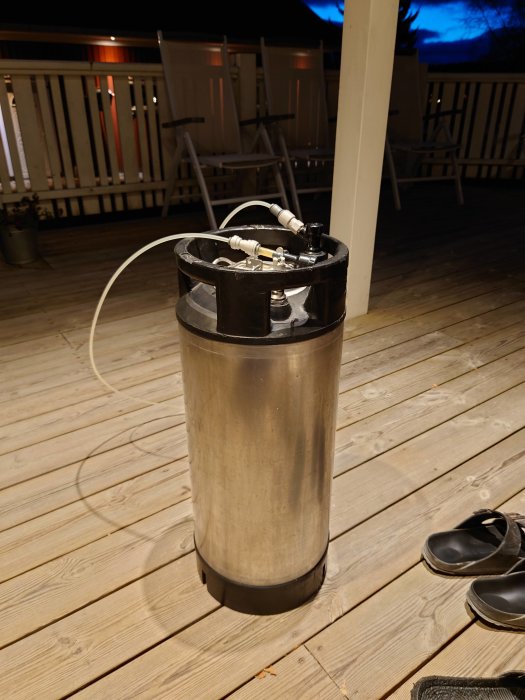 En rostfri cylinderformad bryggkärl på en träaltan med slangar och kopplingar på kvällen.