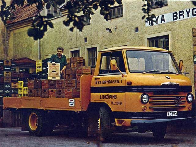 Gul dryckesdistributionsbil lastad med backar av drycker framför en byggnad, med en man som arrangerar lådorna.