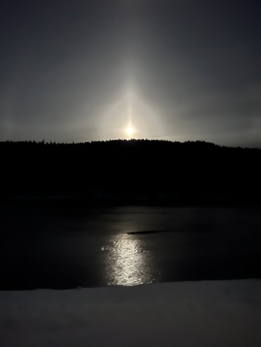 Nattbild med månuppgång över skog och reflektion i vatten, med snö i förgrunden.