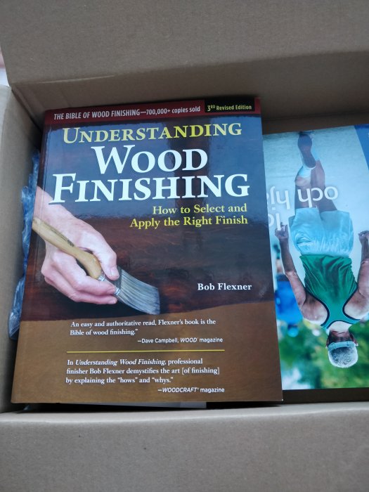 Bok "Understanding Wood Finishing" av Bob Flexner i en kartong, behandlar träfinish och metod.