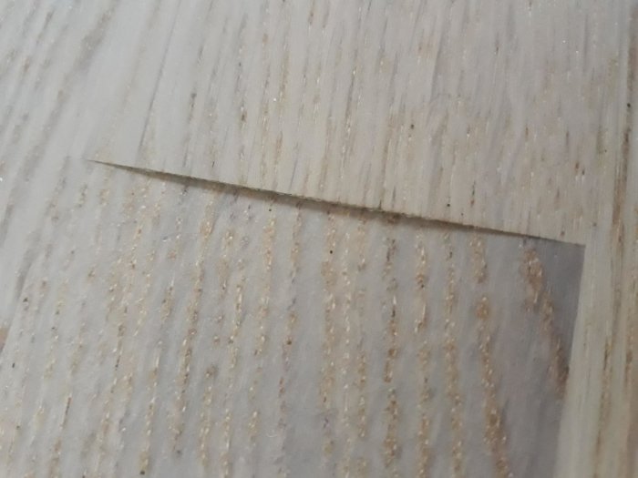 Närbild på skadad parkett där en plankdel är nedsänkt vid kanten skapande en ojämn yta.