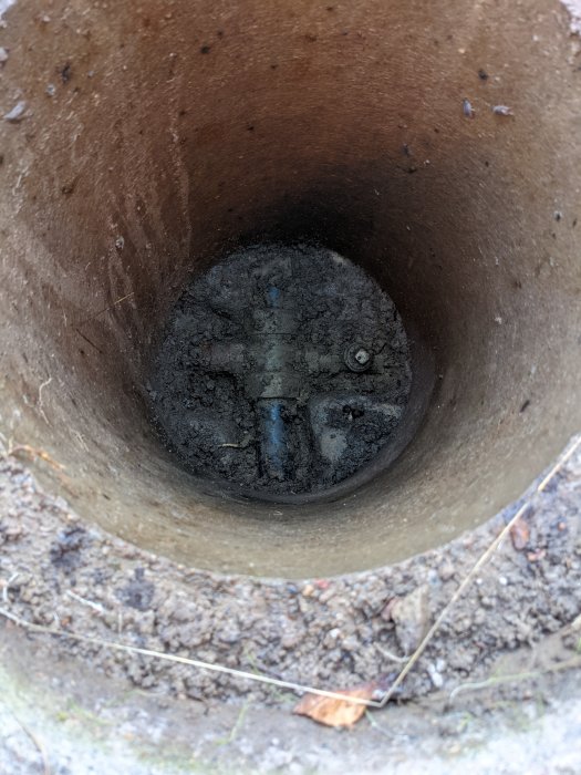 Gammal betongbrunn med mässingskoppling och PEM-rör i botten, tecken på åldrande och tidigare användning.