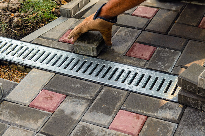 Installation av markränna i stenbelagd gångväg av en person som lägger plattor.