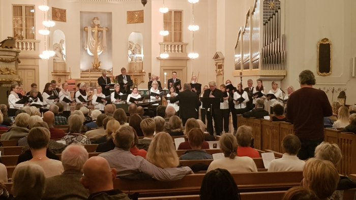 Kör uppträder vid konsert i kyrka med publik som lyssnar.