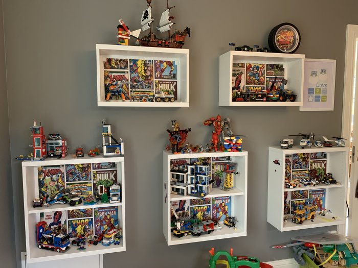 Lekrum med vita hyllor fyllda med Lego byggsatser och affischer av superhjältar på väggen.