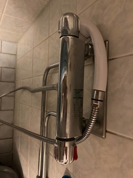 Kromad termostatblandare monterad på kakelvägg i badrum, tillhörande slangar synliga.
