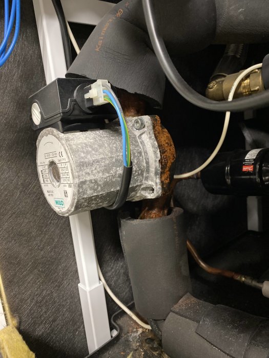 Innervy av värmepump med T1 elektronisk komponent, ledningar och rostiga rör.