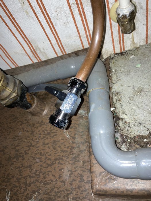 VVS-installation med kopparrör, kulventil och äldre kran utan handtag på våtrumsgolv.
