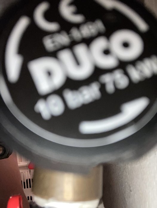Närbild på suddig del av ett objekt med texten "DUCO," indikerar trångt utrymme för fotografering.