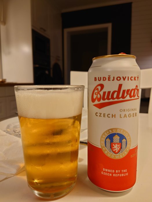 Ett glas med öl och en Budvar-ölburk står på ett bord.