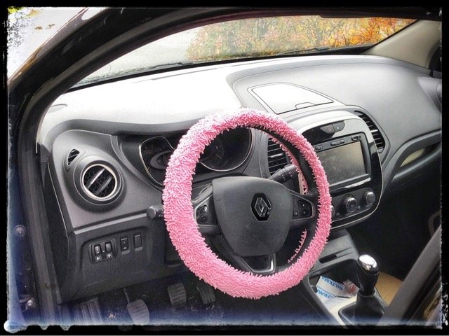 Ratt i en fransk bil med rosa rattöverdrag, set från förarsätet.