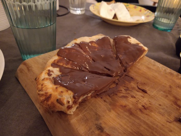 Hembakat glutenfritt bröd med smält choklad ovanpå, serverat på ett träskärbräde.