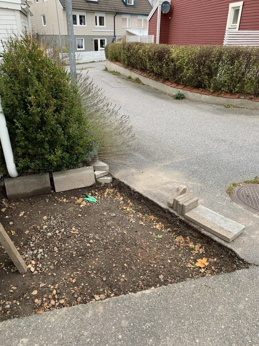 Ett grävt hål vid en husvägg och trottoarkant som förbereds för marksten och cykelparkering.