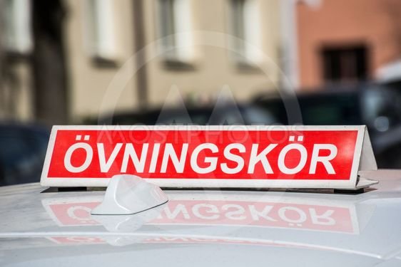 Röd skylt med texten "ÖVNINGSKÖR" på en bil som antyder att en elevförare övar på körning.