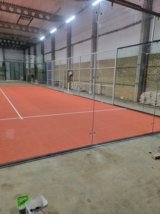 Nybyggd padelbana inomhus med röd markbeläggning och glasväggar.