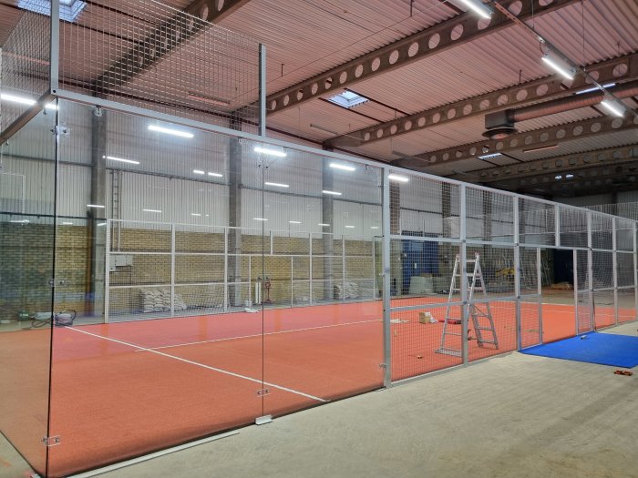 Nybyggd padelbana inne i en industrihall med röd konstgräsmatta och omgivande nät.