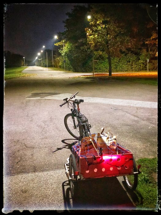 Cykel med släpvagn belyst av röda LED-ljus innehållande matkassar på en mörk väg.