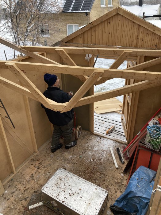 Person demonterar takstolar i trä på ett halvt nedrivet förråd under vintersäsong.