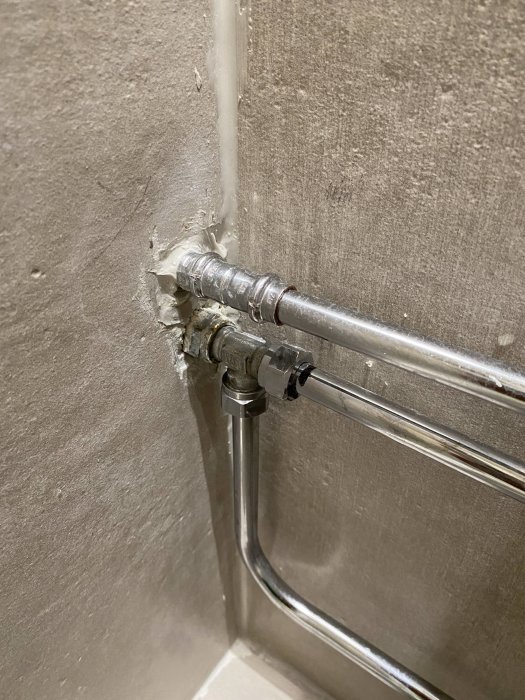 Rörinstallation i badrum med synliga sprickor och utan täckbricka vid vägggenomföring.